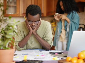 Stressed Young African Male Doing Paperwork At Home, Holding Hands On Head Having Frustrated And Puzzled Look While Reading Notification From Bank In Front Of Him, Failed To Pay Loan In Time